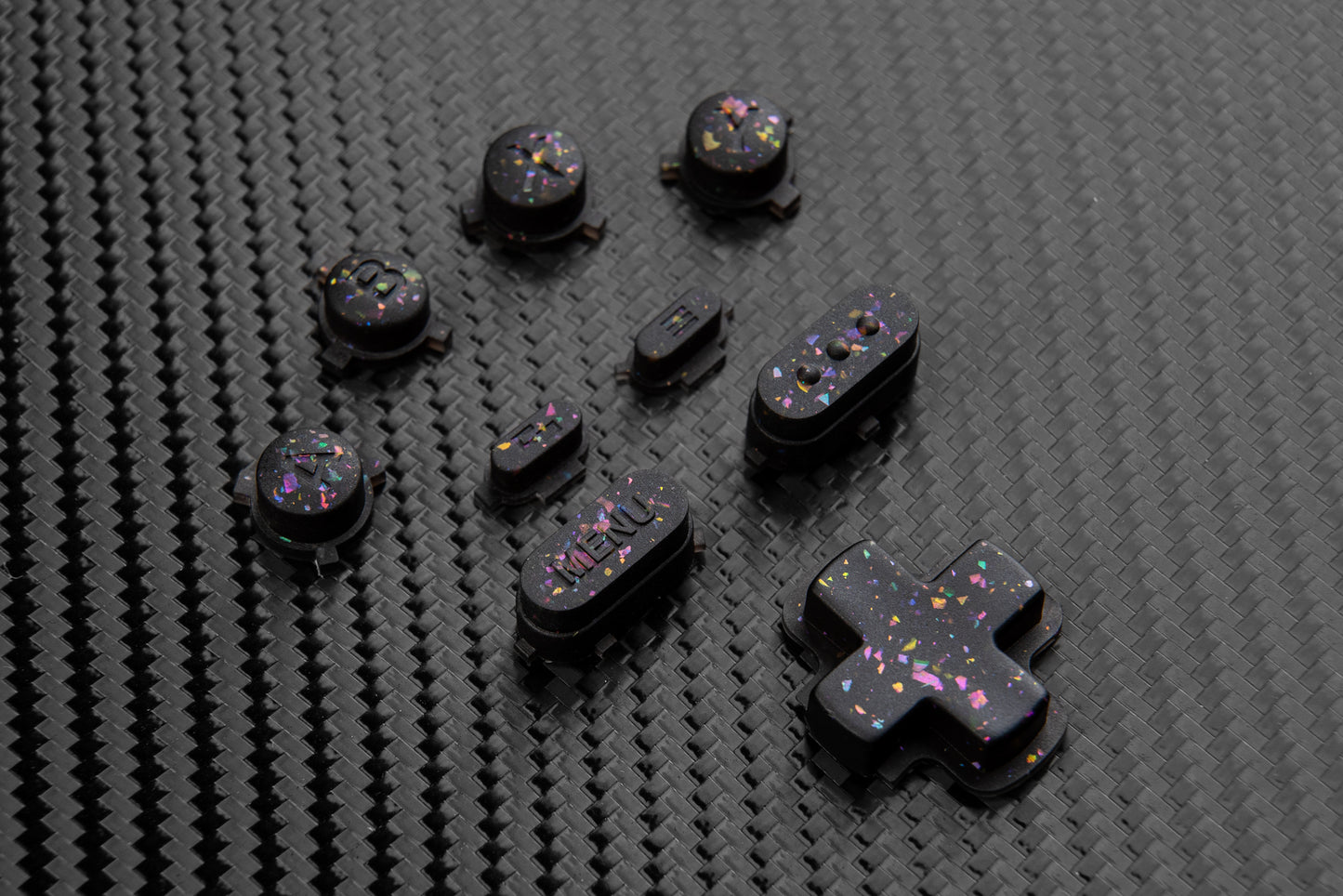 Steam deck buttons on a carbon fiber backdrop. Black buttons with metallic shards of colors mixed throughout.