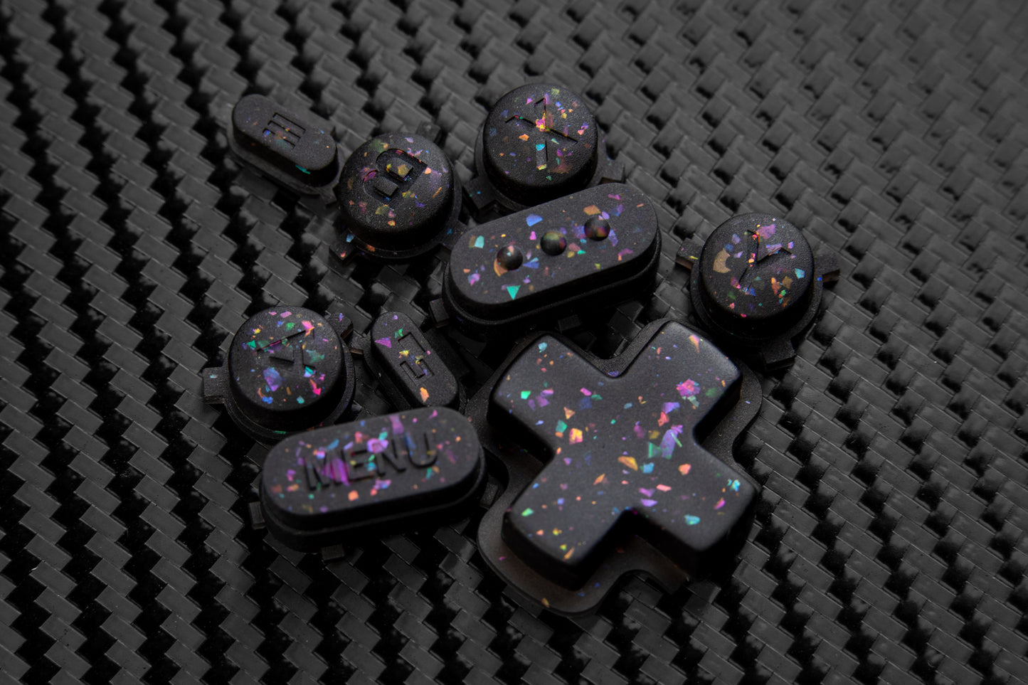 Steam deck buttons on a carbon fiber backdrop. Black buttons with metallic shards of colors mixed throughout.