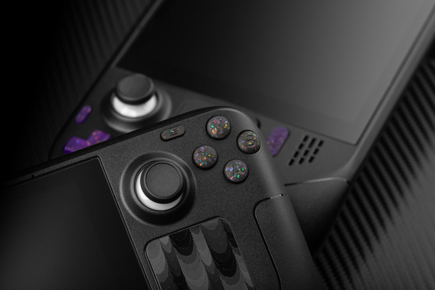 steam deck with party black abxy buttons leaning against a steam deck with purple buttons installed