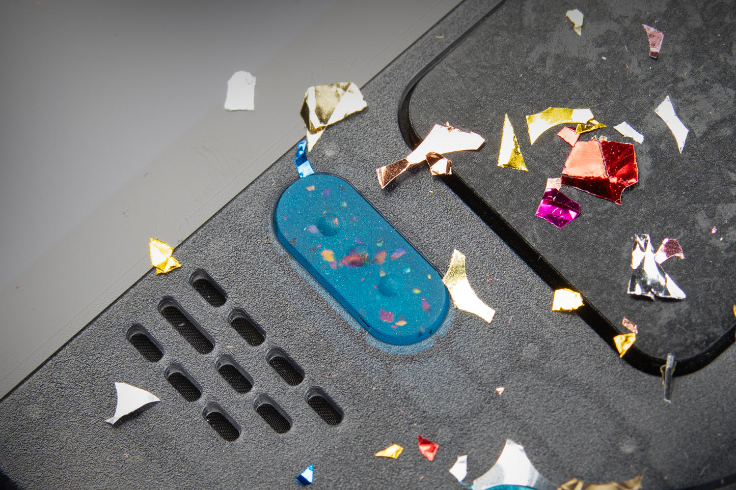 Close up of party blue "3 dots" button of a steam deck. Confetti on top of steam deck.