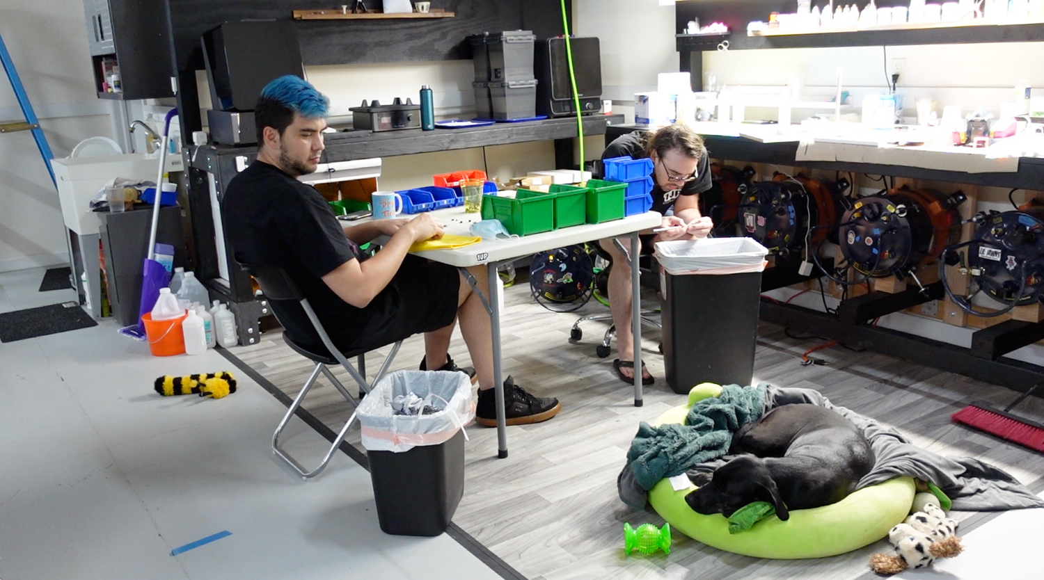 two people and a dog sitting at a table working on stuff