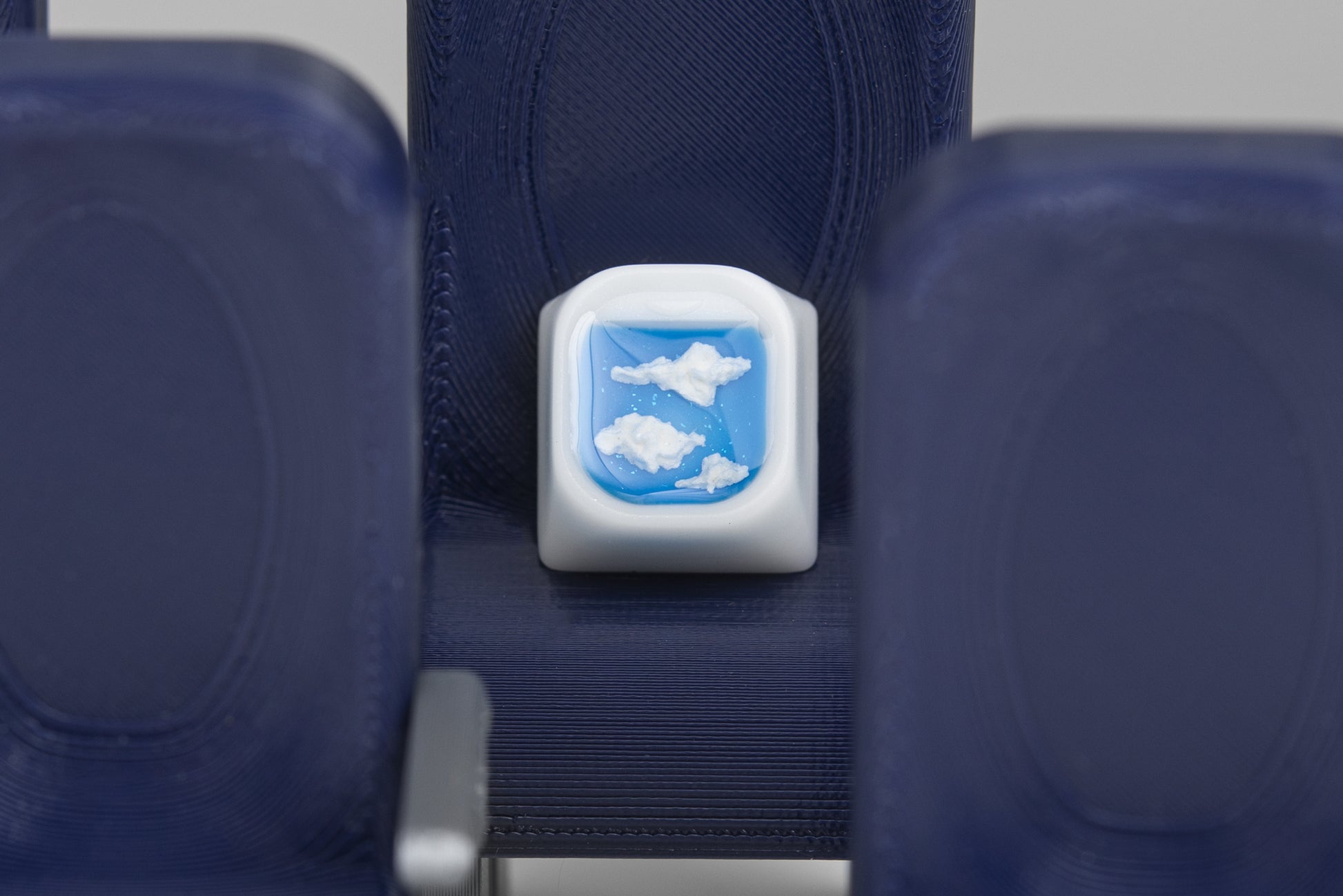 airplane window artisan keycap, clouds. Keycap sitting in an airplane seat