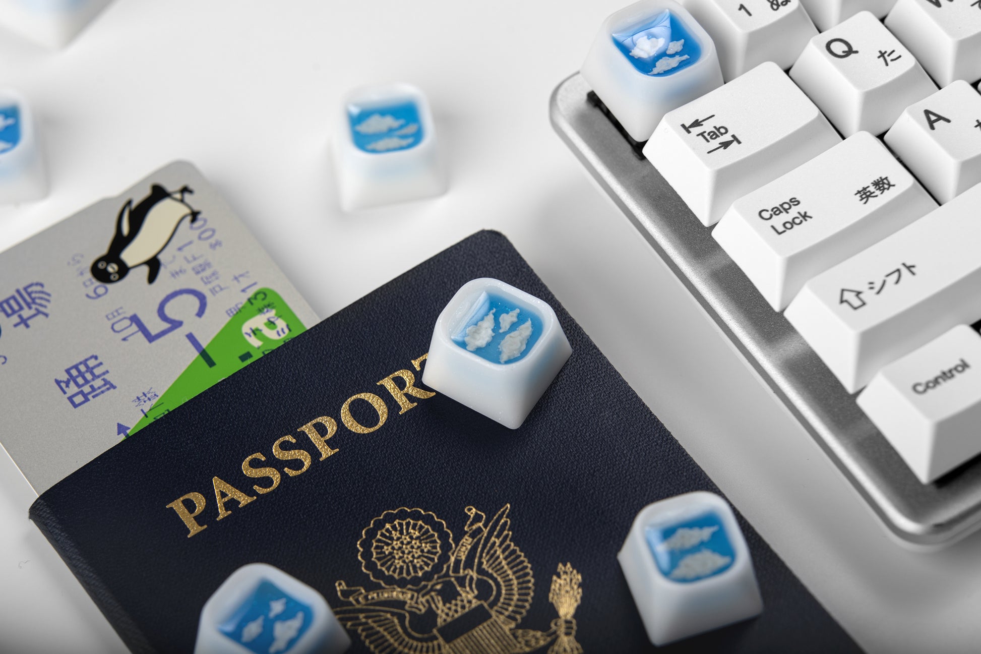 Airplane window artisan keycaps shown sitting on a passport, keyboard on right side of image