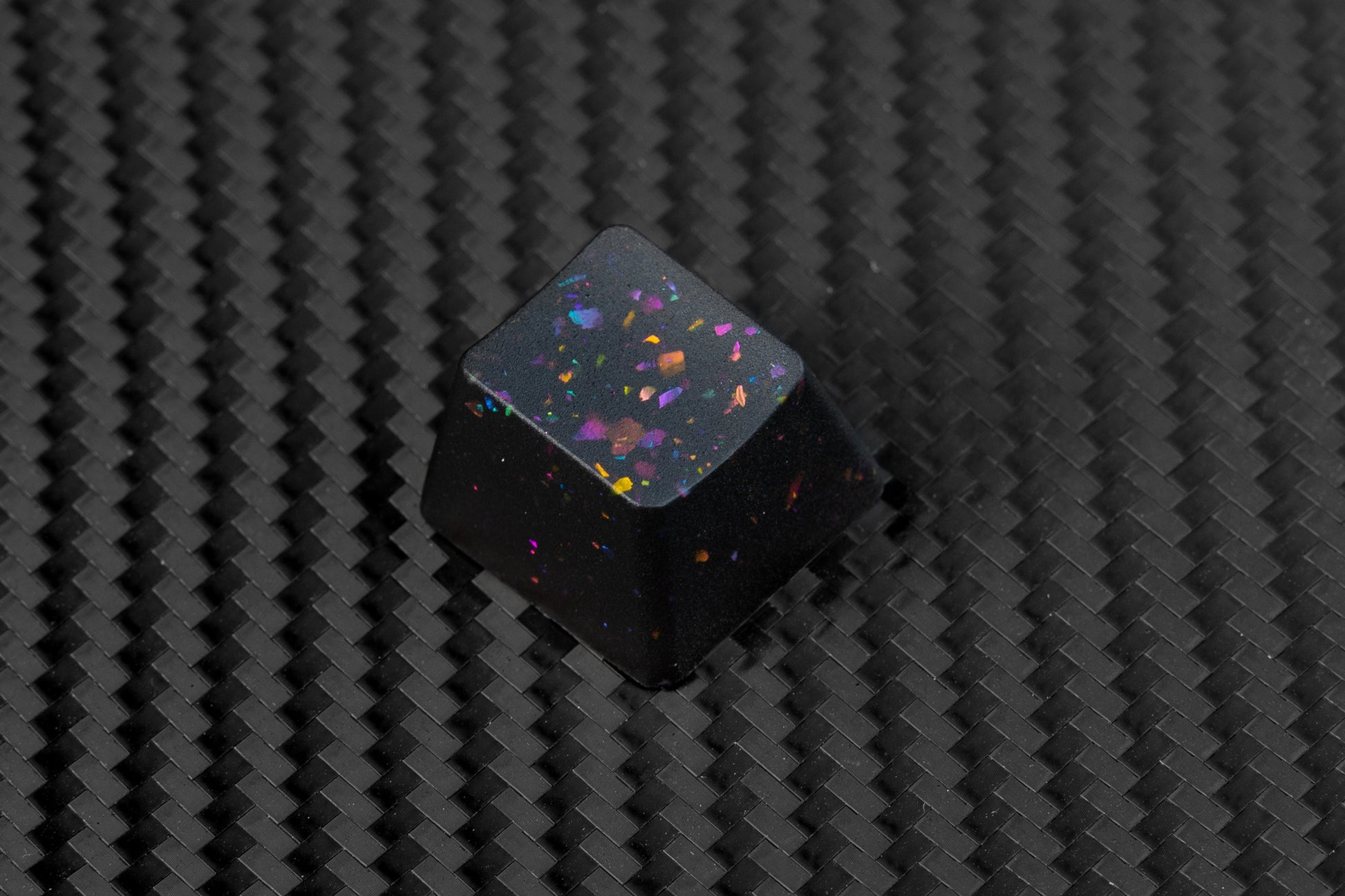 Mechanical keyboard key in party black. Party black metallic shards of color mixed into black buttons.  Keycap on carbon fiber background