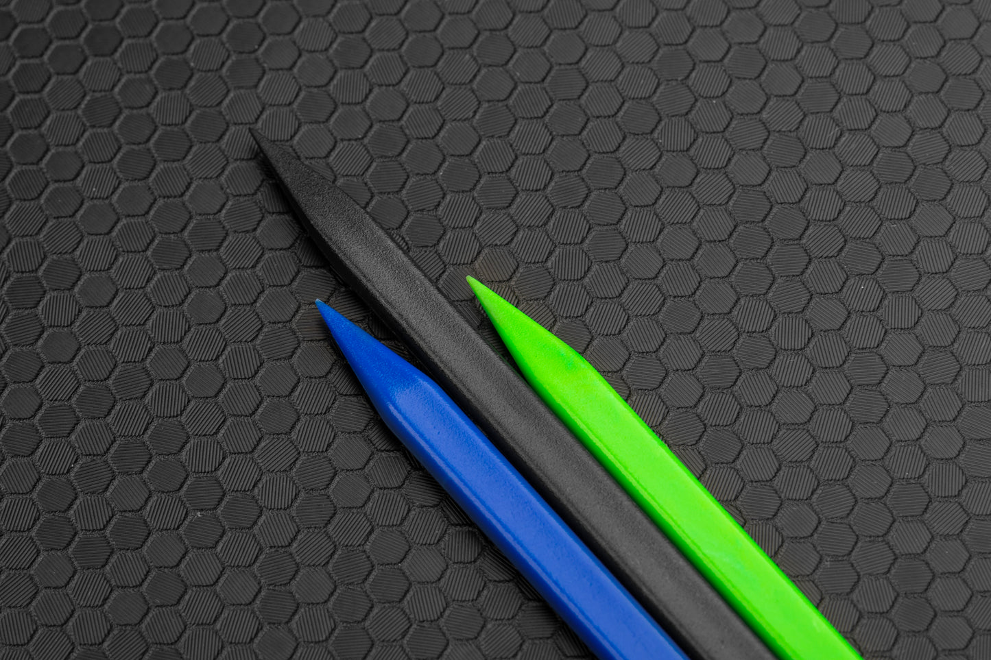 Pointy tips of spudgers. Blue on left, black middle, green on right. Hex background. 