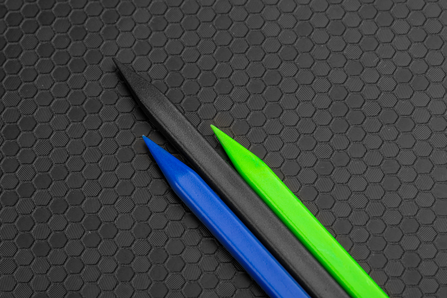 Pointy tips of spudgers. Blue on left, black middle, green on right. Hex background. 