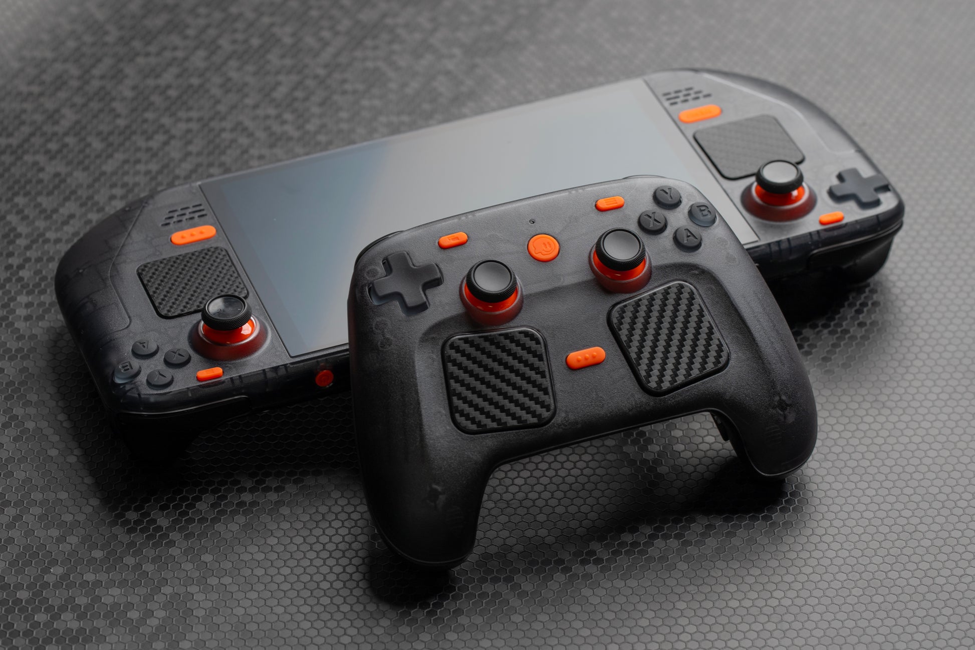 Steam controller leaning on steam deck. Both have a smoked black shell with orange accent buttons installed. 